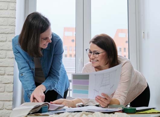 Two women choosing fabrics for curtains. Females textile designer, decorator and client watch palettes with fabrics, choose model and fabric